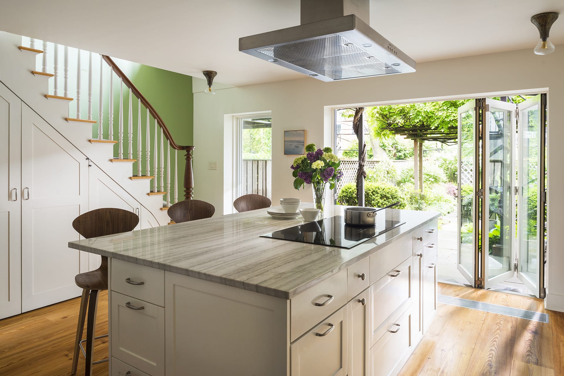 Garden level kitchen with staircase to the left, white millwork island, and NanaWall leading out to the back garden.